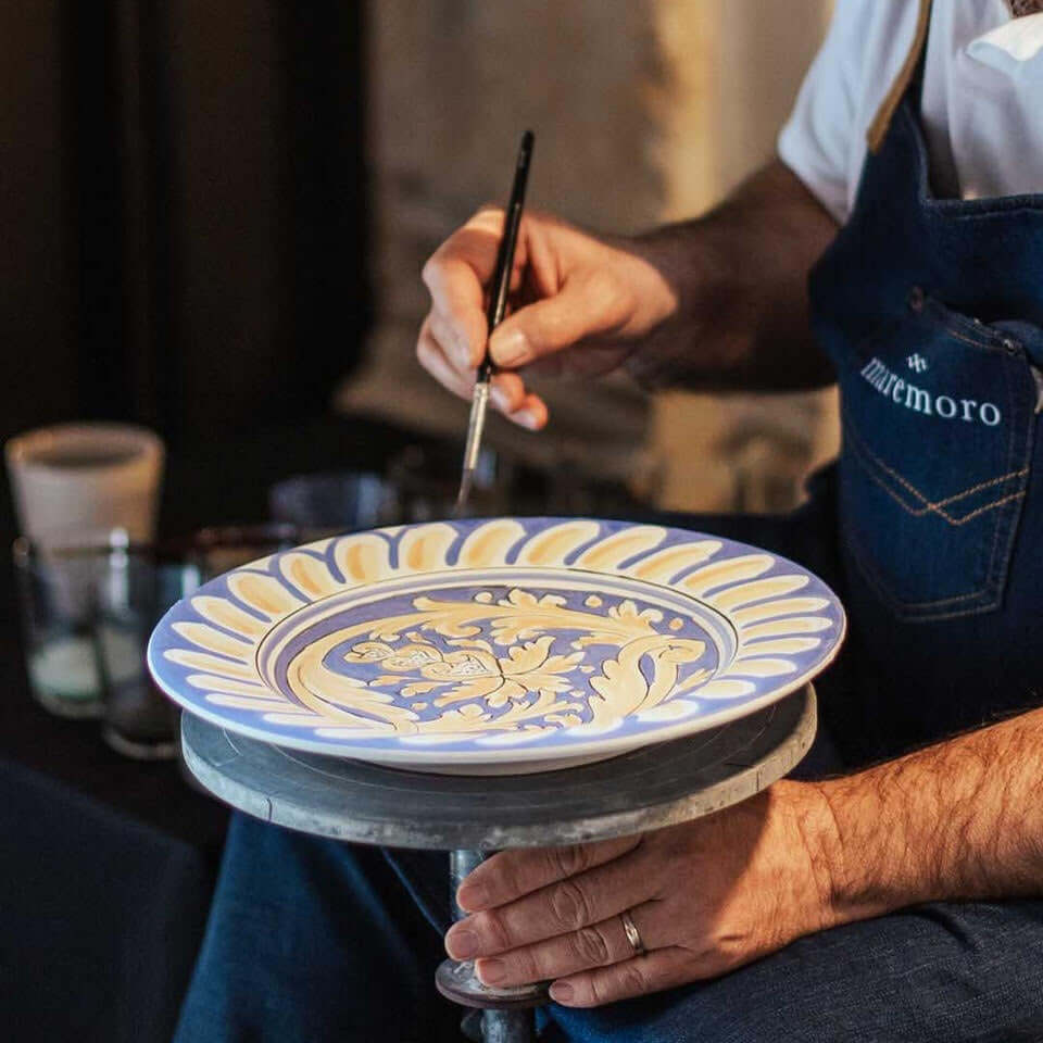 Artisan painting a handcrafted Sicilian dinner plate with intricate blue and yellow designs in Caltagirone.